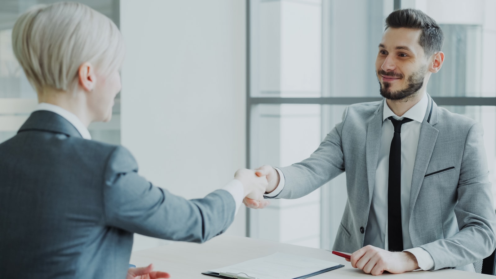 Two colleagues shaking hands across a desk in an office